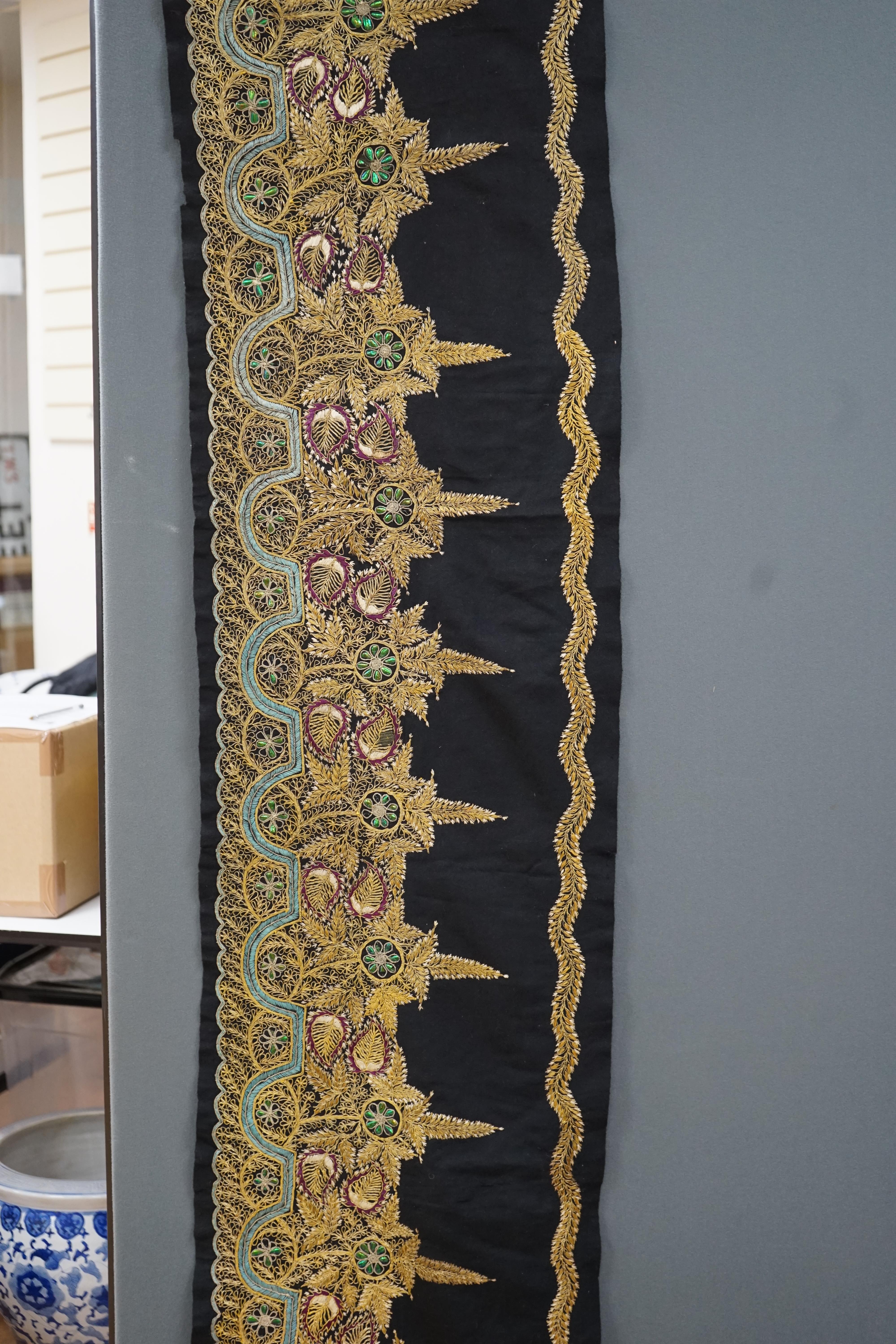 An Indian black felt panel embroidered with mostly gold thread, some coloured silks and beetle wing ornamentation, possibly a border to a larger panel, 256cm long. Condition - good